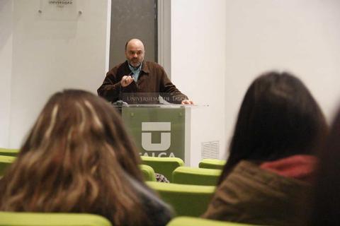Un ponente está hablando frente a un público en un auditorio universitario.
