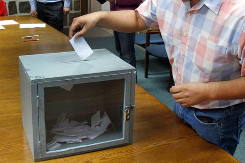 Un hombre está depositando un voto en una urna transparente durante un proceso electoral.