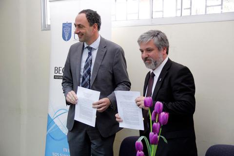 Dos hombres sosteniendo documentos en una ceremonia de firma.