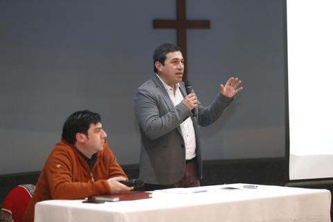 Dos hombres participan en una presentación mientras uno de ellos habla con un micrófono.
