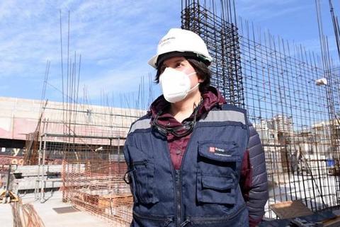 Una persona con casco y mascarilla se encuentra en un sitio de construcción rodeada de estructuras metálicas.