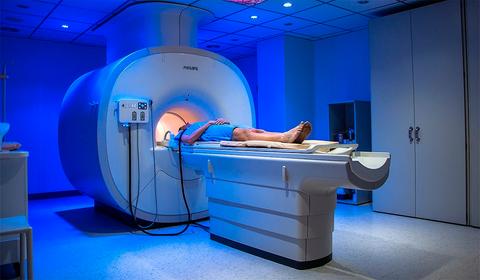 Una persona se encuentra acostada en una máquina de resonancia magnética en una sala de procedimiento médico iluminada con luz azul.