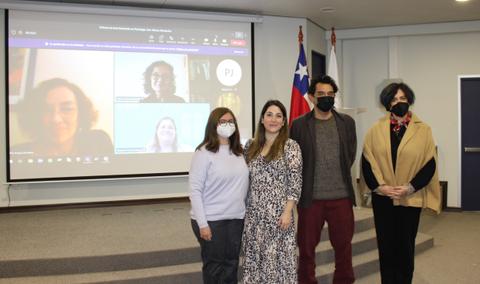 Un grupo de cuatro personas posando en una sala de reuniones con pantallas y banderas al fondo.