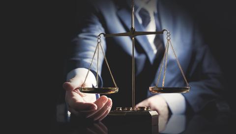 Una persona vestida de traje presenta una balanza de la justicia.