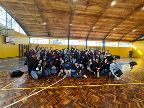 Un grupo grande de personas sonrientes se reúne en un gimnasio con pisos de madera.