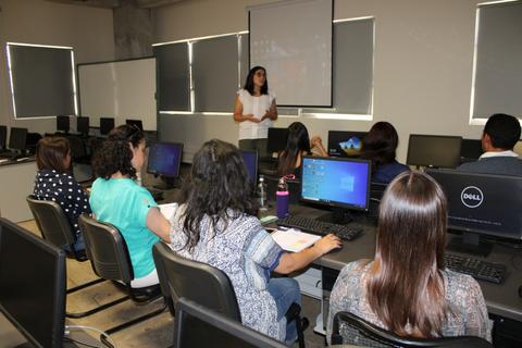 Una mujer está dando una presentación frente a un grupo de personas en un aula con computadoras.