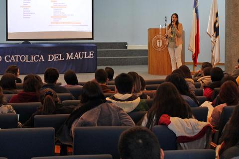 Una presentadora habla frente a una audiencia en un auditorio universitario.