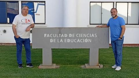 Dos hombres posan junto a un letrero que indica la Facultad de Ciencias de la Educación.