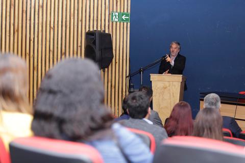 Un orador se encuentra en un podio hablando frente a una audiencia en un auditorio.