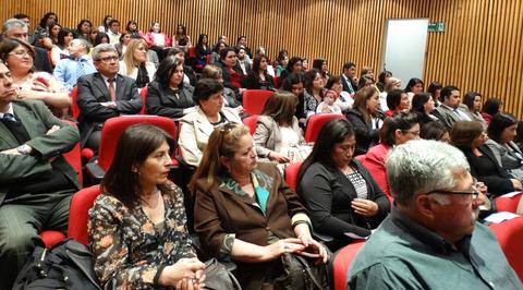 Una reunión en un auditorio con un gran número de personas sentadas en sillas rojas.