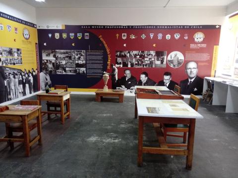 Una sala de museo dedicada a los profesores y profesoras normalistas de Chile, con mesas de trabajo y una pared decorada con fotografías históricas.
