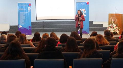 Una oradora se presenta frente a un público en un evento educativo.