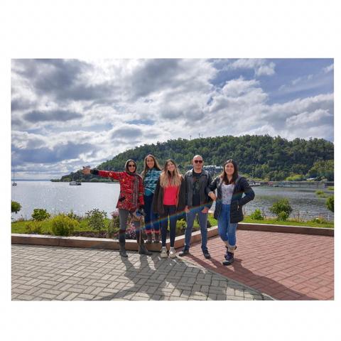 Grupo de seis personas posando sonrientes frente a un lago y un paisaje montañoso.