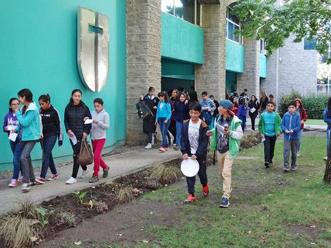 Un grupo de niños camina por un área verde frente a un edificio escolar.