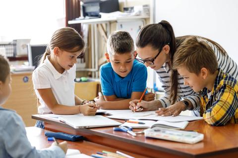 Un grupo de niños y una maestra están trabajando juntos en una actividad en un salón de clases.
