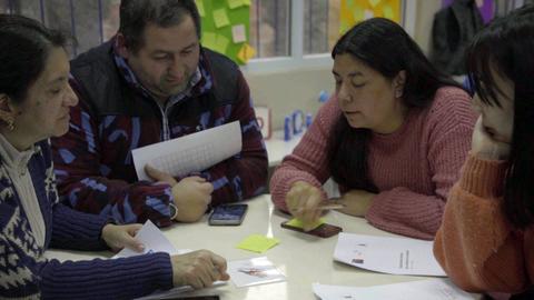 Un grupo de personas discute y trabaja en conjunto alrededor de una mesa con documentos y dispositivos móviles.
