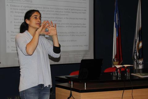 Una mujer está dando una presentación frente a una audiencia, utilizando gestos para ilustrar sus puntos.