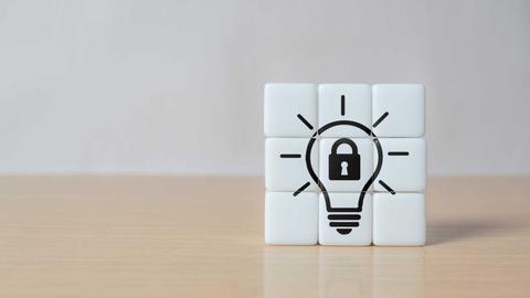 Un cubo de puzzle blanco con una bombilla y un candado dibujados en el centro, simbolizando ideas protegidas.