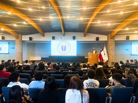 Una conferencia con un orador frente a un auditorio lleno de estudiantes.