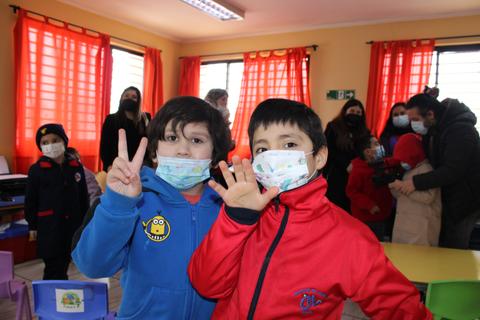Dos niños en un aula con mascarillas, posando y sonriendo para la cámara.