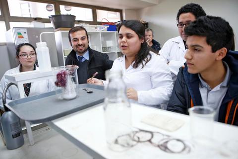 Un grupo de estudiantes y profesores participan en una actividad de laboratorio mientras una estudiante explica un experimento.