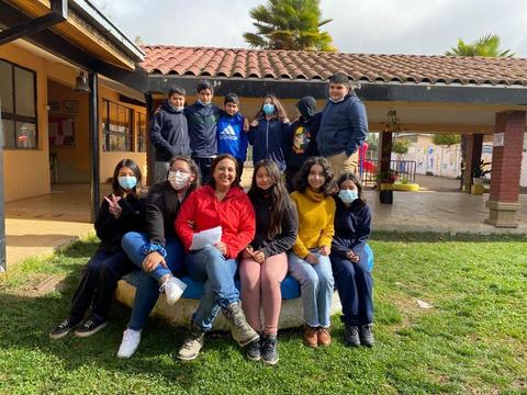 Un grupo de estudiantes posando junto a una docente en un entorno escolar con máscaras faciales.