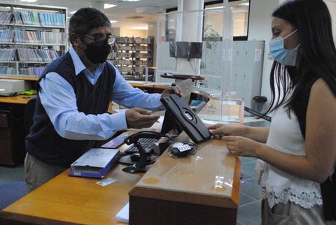 Un hombre y una mujer conversan en una biblioteca mientras manejan un dispositivo en un escritorio.