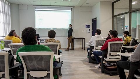 Una clase en un aula con un profesor y varios estudiantes prestando atención.