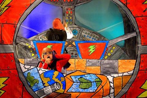 Un niño disfrazado como astronauta juega en una nave espacial de cartón decorada.