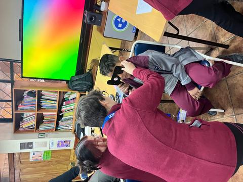 Un grupo de personas interactúa en un aula con un monitor colorido de fondo.