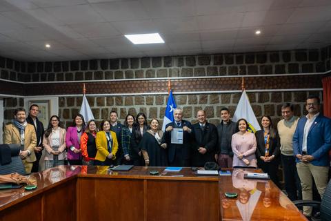 Un grupo de personas se reúne en una sala, mostrando un documento, con banderas de Chile en el fondo.