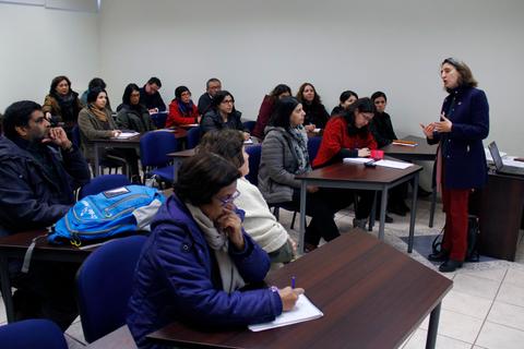 Un grupo de personas en un aula escuchando a una presentadora.