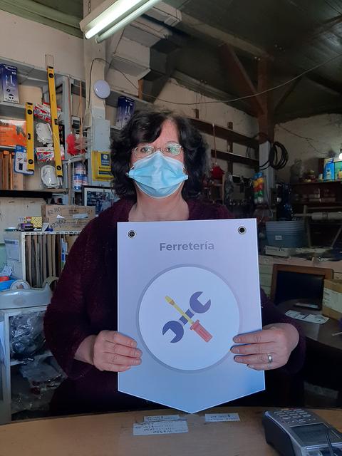 Una mujer con mascarilla sostiene un cartel que dice 'Ferretería'.