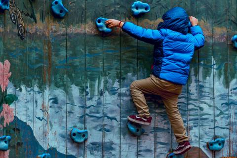 Un niño sube por una pared de escalada con un abrigo azul.
