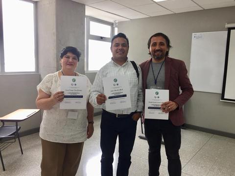 Tres personas sonrientes sosteniendo certificados en un ambiente de oficina.