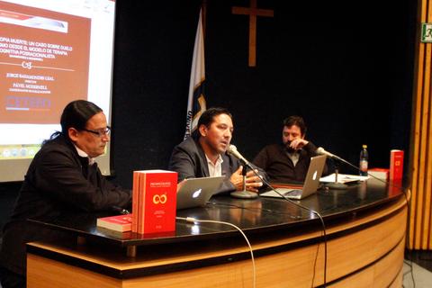 Una conferencia en la que tres hombres discuten sobre un tema frente a un público.