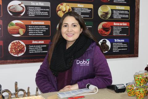 Una mujer sonriente se encuentra en un puesto de venta de alimentos saludables.