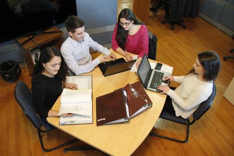 Un grupo de cuatro personas trabaja en una mesa con laptops y documentos.