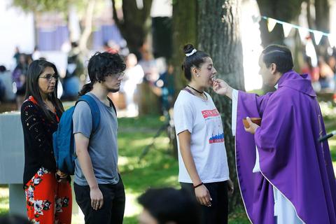 Un grupo de personas se acerca a un sacerdote en un ambiente al aire libre.