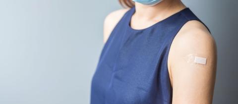 Una persona con una mascarilla muestra su brazo izquierdo después de haberse vacunado.