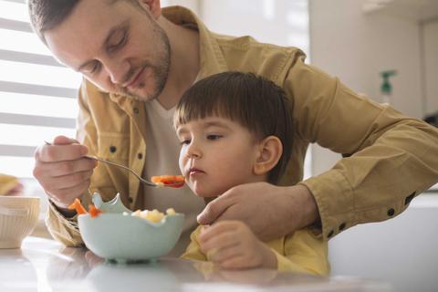 Un padre alimenta a su hijo pequeño en la cocina.