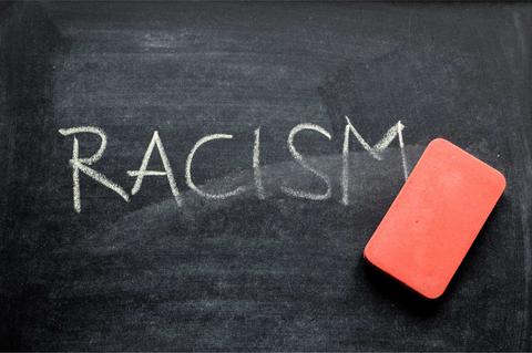 Una pizarra negra con la palabra 'RACISM' escrita en tiza y una goma de borrar roja a un lado.