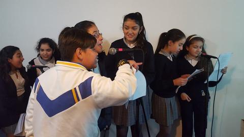 Un grupo de niños y niñas cantando en un micrófono durante una actividad escolar.