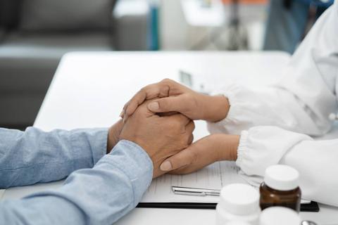 Dos manos se unen en un gesto de apoyo y empatía durante una consulta médica.