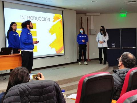 Un grupo de presentadores expone información frente a una audiencia en un aula.