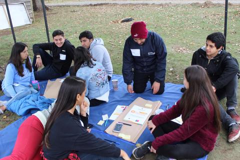 Un grupo de jóvenes discuten y trabajan en un proyecto al aire libre sobre una manta.