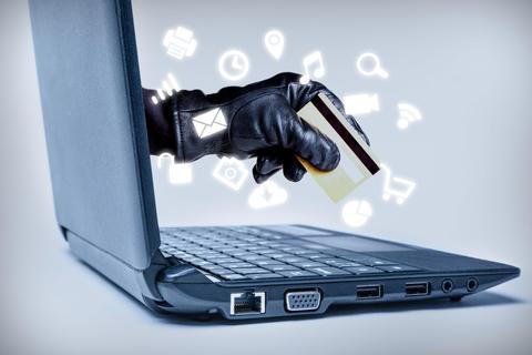 Una mano con un guante negro sostiene una tarjeta de crédito mientras se asoma desde una laptop, simbolizando un posible robo en línea.
