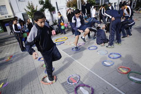 Un grupo de niños juega en un espacio al aire libre con aros de colores en el suelo.