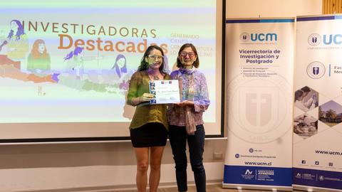 Dos mujeres posando juntas con un certificado en un evento de reconocimiento a investigadoras.