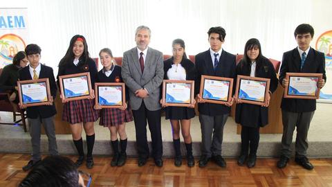 Un grupo de estudiantes posando con certificados de reconocimiento junto a un adulto en un evento.
